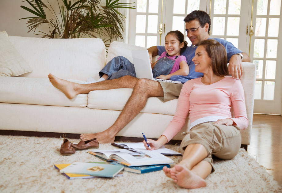 family sitting casually on the couch and on the floor looking and smiling at a white laptop